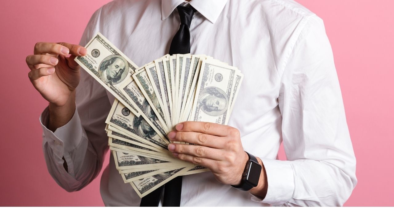Homem de camisa e gravata segura várias notas de dólar