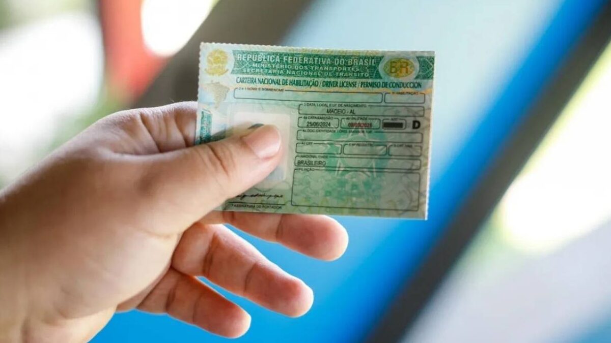 Mão segurando uma Carteira Nacional de Habilitação (CNH) em primeiro plano.
