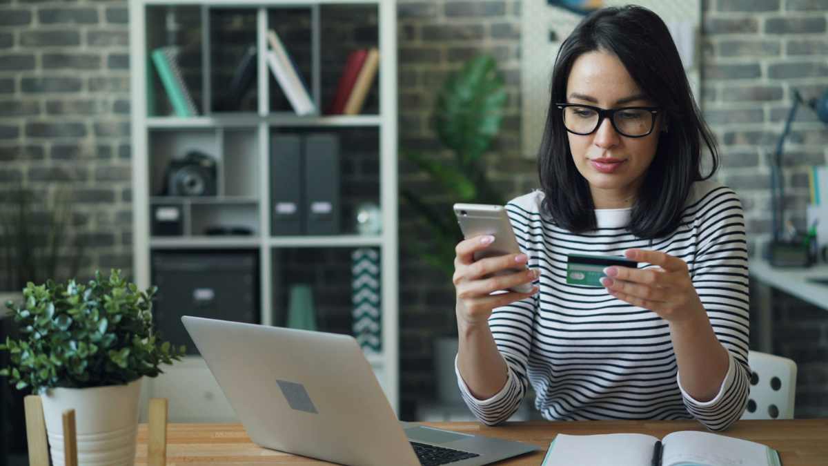 Retrato de uma jovem mulher efetuando um pagamento com cartão de crédito usando seu smartphone