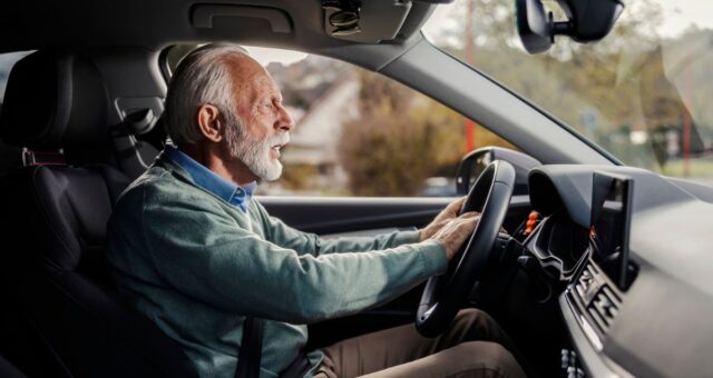 Vista lateral do homem sênior sério buzinando no trânsito.