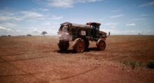 Trabalhador rural dirige trator espalhando fertilizante em campo de soja