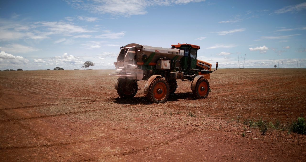 Trabalhador rural dirige trator espalhando fertilizante em campo de soja
