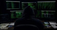 Hacker observa telas de computadores. Sobre a mesa, diversos documentos para a aplicação de golpes e fraudes.