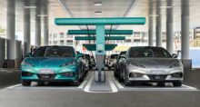 Fila de carros elétricos Denza estacionados em uma área coberta de recarga, conectados a carregadores rápidos dispostos em série