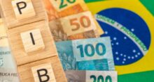 Foto de stock de A palavra PIB (Produto Interno Bruto) escrita em cubos de madeira com dinheiro real brasileiro em amarelo, bandeira verde do Brasil. Língua Portuguesa do Brasil