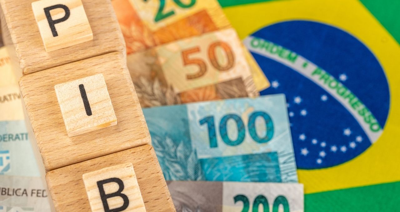 Foto de stock de A palavra PIB (Produto Interno Bruto) escrita em cubos de madeira com dinheiro real brasileiro em amarelo, bandeira verde do Brasil. Língua Portuguesa do Brasil